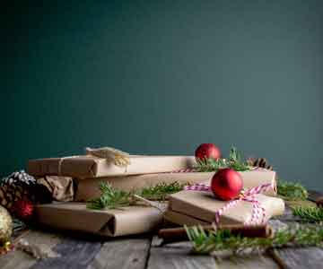 Christmas gifts wrapped in brown paper and string with ornaments on a wooden desk. 