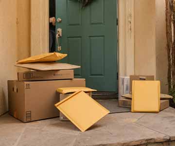 Multiple packages stack on top each other by a front door that is being opened.