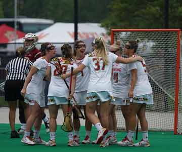 A team of women's lacrosse hugging at the goal post.
