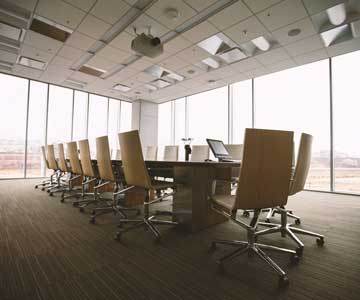 An empty board room with long table, chairs, and a view from the windows.