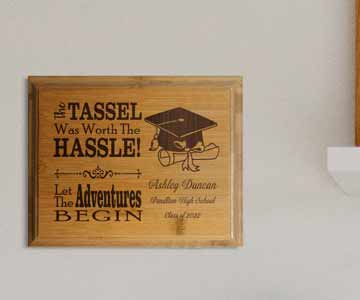 A bamboo plaque hanging on the wall. The plaque says The tassel was worth the Hassle