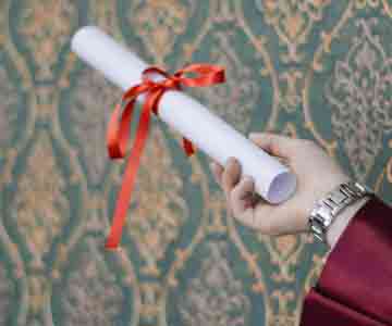 A hand holds a rolled-up diploma tied with a red ribbon.