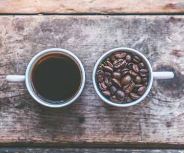 Two coffee mugs, one filled with liquid coffee, the other filled with coffee beans.
