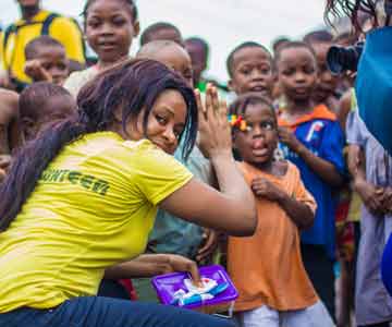 Young Happy Woman With Volunteer Shirt High Fiving Group Of Kids.