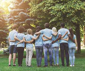 A group of young volunteers interlocking arms and looking at trees.