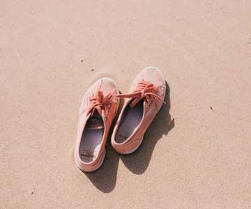 A Pair Of Woman's Pink Shoes Resting On The Sandy Beach.