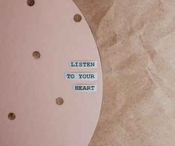 Pink rounded background with three small square stainless signs that say “Listen to Your Heart.” 