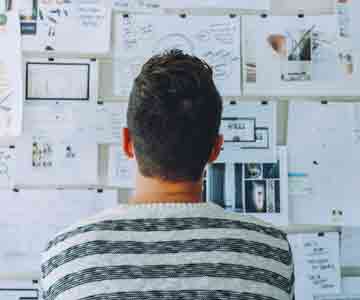 Facing a wall of design sketches, person seen from behind.