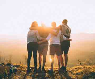 Four friends hug atop a mountain as the sun rises.