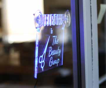 A custom cut acrylic sign, lite in blue, hanging from a window.