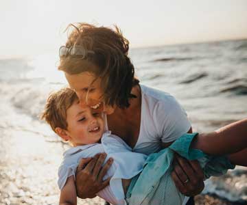 A mother spinning her son around on the beach.