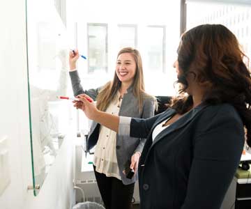 Happy Business Woman Writing On Dry Erase Board in Conference Room. 