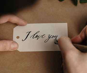 One hand holds a small tag while the other writes “I love you.”