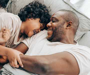 A father and son laying in bed together smiling.