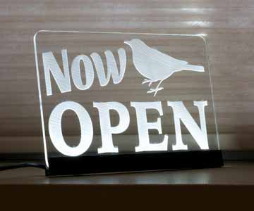 A LED Light up Sign with Now Open and a bird engraved on the run, lit up in white light.