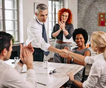 A group of colleagues sitting at a meeting table, appreciating all the hard work the office has been putting in.