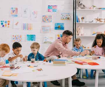 Teacher guiding kids around a round table in a classroom setting.