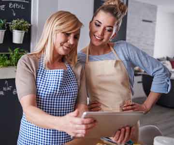 Two women standing together looking at a digital tablet for their business.