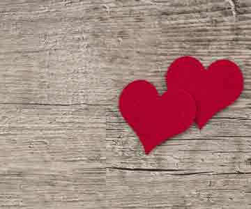 Two red hearts resting on a wooden surface