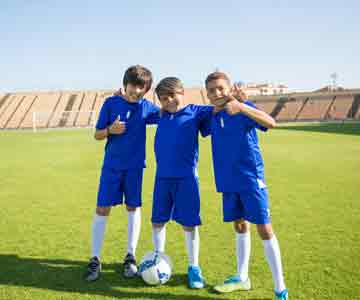Three young kids in blue uniforms on a soccer field.