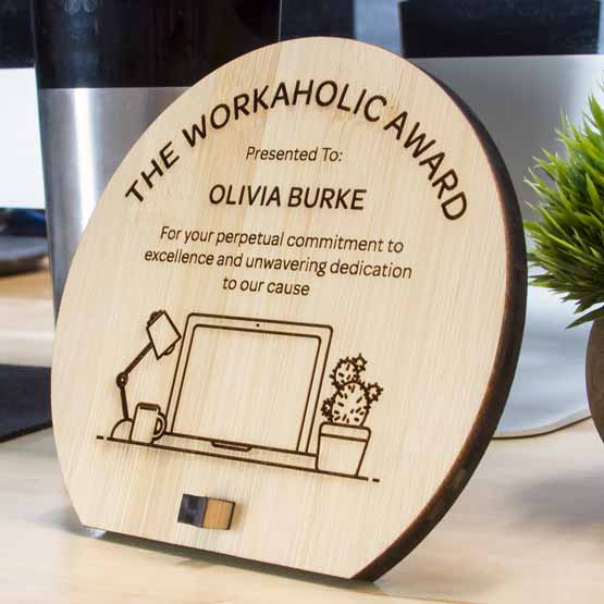 Custom Engraved Bamboo Award In Unique Shape Near Computer And Plant.