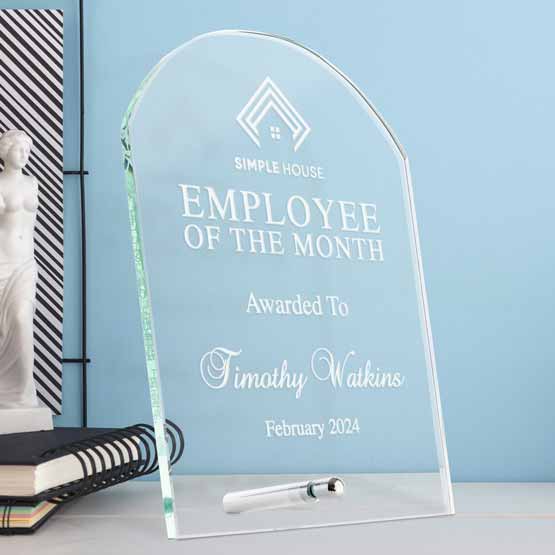 Custom Tombstone Shaped Glass Award For Employee Of The Month Standing On White Office Desk Via Silver Pin Beside Notebooks