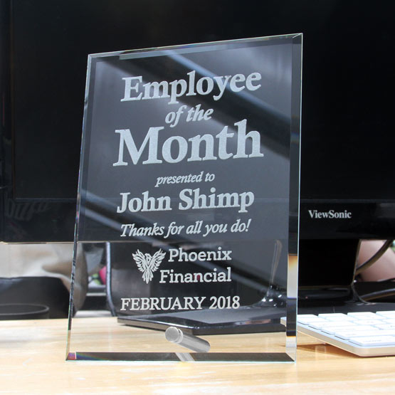 Custom Glass Award For Employee Of The Month Standing Via Silver Pin On Busy Work Desk With Laptop And Keyboard