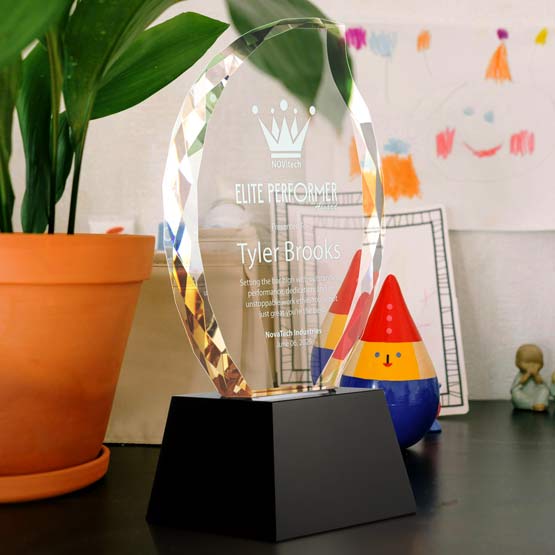 Custom Faceted Flame Glass Award For Elite Performer With Black Base Standing On Desk With Potted Plant And Kids Artwork