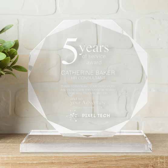 Custom Faceted Octagon Glass Award For Years Of Service With Glass Base On A Wood Shelf With Plant Against White Wall
