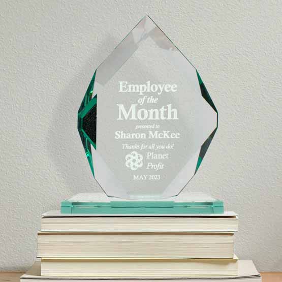 Custom Royal Diamond Glass Award For Employee Of The Month With Glass Base Standing On Stack Of Books Against White Wall