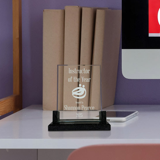 Custom Faceted Rectangle Glass Award For Instructor Of The Year With Ornate Black Base On White Office Desk With Laptop