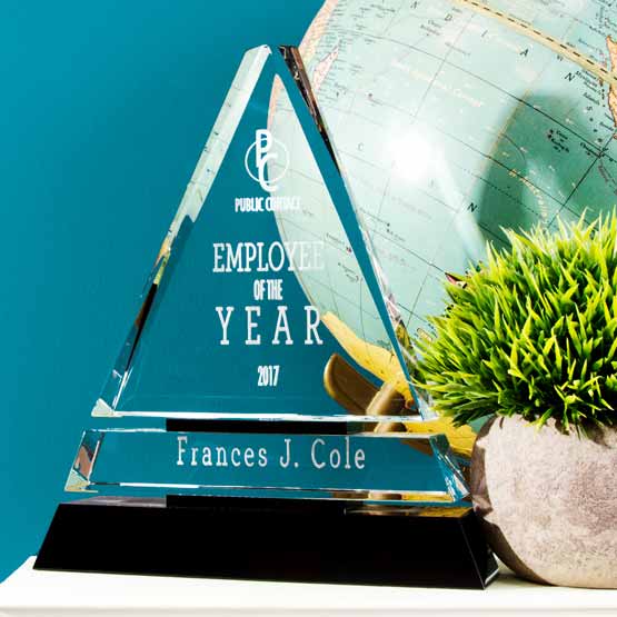Custom Triangle Shaped Glass Award For Employee Of The Year With Black Pedestal Base On White Dresser With Plant And Globe