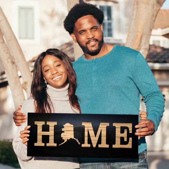 Couple Outside Holding A Custom Bamboo And Black Acrylic Sign With Custom State Shape Inside The Word Home