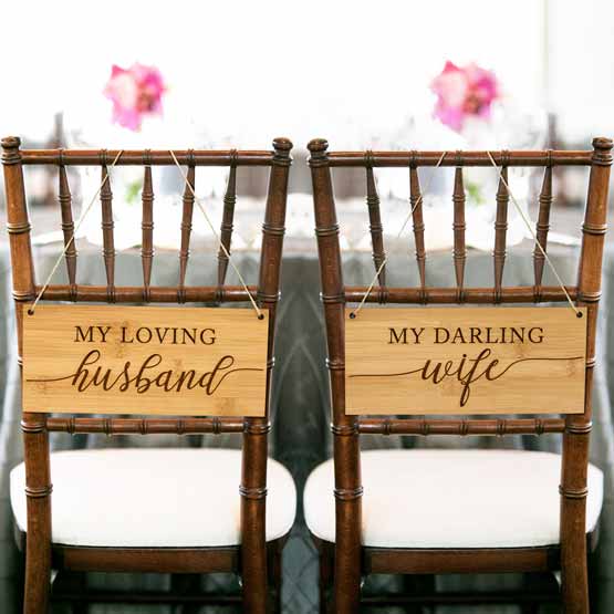 Pair Of Custom Bamboo Wooden Chair Signs Featuring My Loving Husband And Wife Text Hanging On Wedding Chairs Near Table