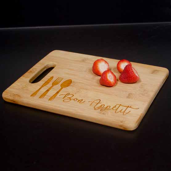 Custom Bamboo Cutting Board Engraved With Utensil Artwork And Bon Appetit Text And Strawberries On Black Kitchen Countertop