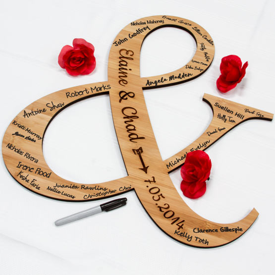 Roses Near Custom Ampersand Shaped Bamboo Sign And Laser Engraved With Couple Names And Date And Marked With Guest Names