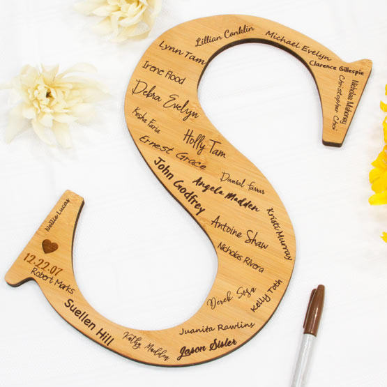 Custom Bamboo Sign With Letter S Shape And Engraved With Heart And Date And Signed By Guests On White Table With Flowers