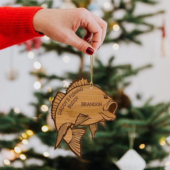Festive Woman Hand Holding Custom Fish Shaped Bamboo Ornament Engraved With Name And Dad Fishing Buddy Text Via Gold String