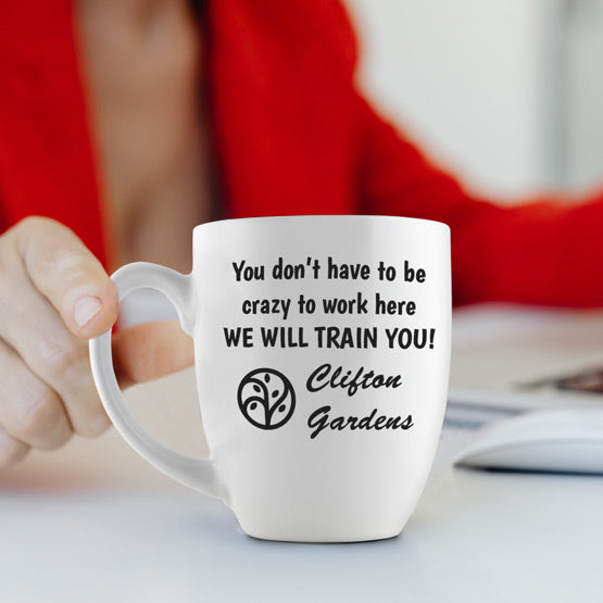 Woman Placing Custom White Ceramic Bistro Mug Engraved With Funny Crazy To Work Here Message And Company Logo Onto Work Desk