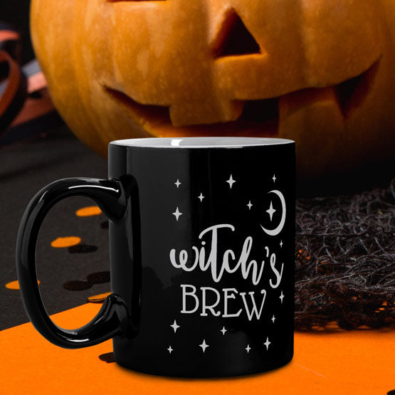 Custom Black Coffee Mug Engraved With Star And Moon Art And Witch’s Brew Text On Table With A Jack O Lantern