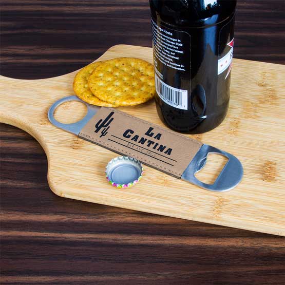Stainless Steel And Light Brown Faux Leather Bottle Opener Engraved With La Cantina Bar Logo On Cutting Board With Beer