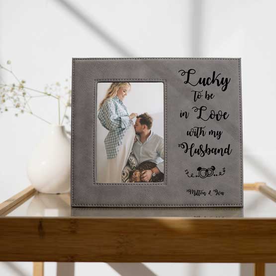 Custom Gray Faux Leather Picture Frame With Romantic Message And Photo Of Man Kissing Pregnant Wife On Side Table With Plant