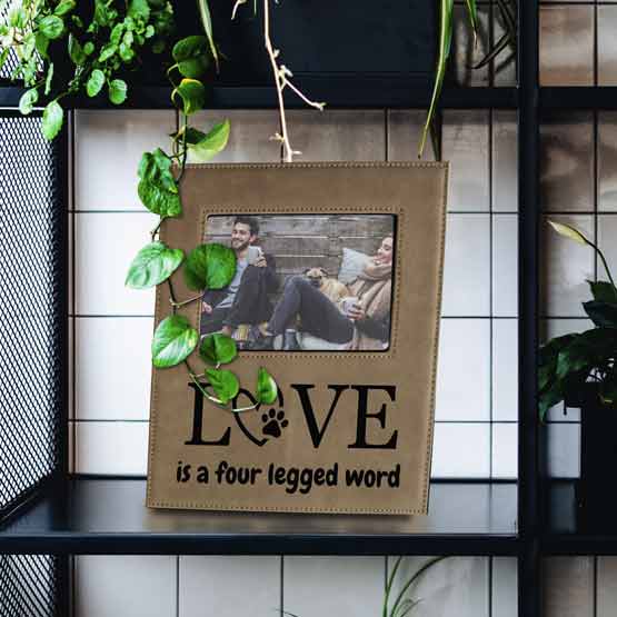 Light Brown Faux Leather Picture Frame With Photo Of Couple And Dog And Engraved With Love Message On Bookshelf With Plants