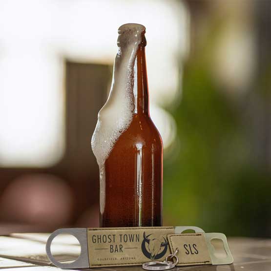 Set Of Custom Light Brown Faux Leather Bottle Opener With Ghost Town Bar Text And A Small Keychain Bottle Opener Near Beer