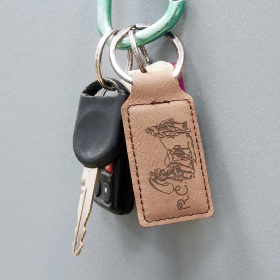 Dark Brown Faux Leather Rectangle Keychain Engraved With Initials And Cowboys Lassoing Cow Artwork Hanging On Wall With Keys