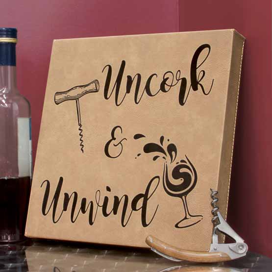 Light Brown Faux Leather Wrapped Square Canvas Engraved With Wine Artwork And Uncork And Unwind On Table With Bottle