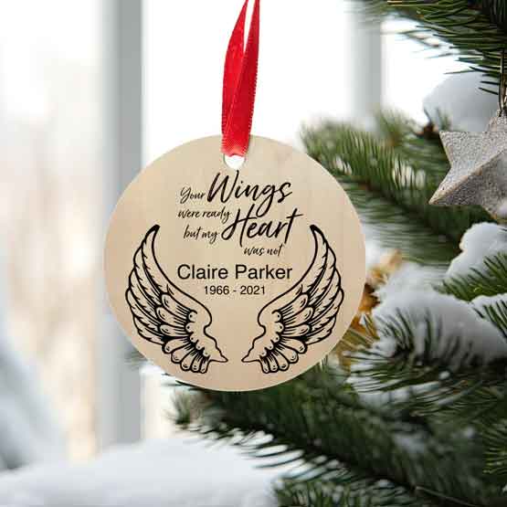 Maple Wood Circle Ornament With Black Printing Of Angel Wings And Memorial Message Hanging On Christmas Tree Via Red Ribbon
