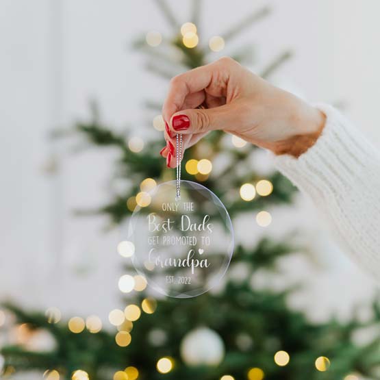 Hand Holding Circle Glass Ornament Engraved With Date And Promoted To Grandma Massage Near Christmas Tree Via Silver String