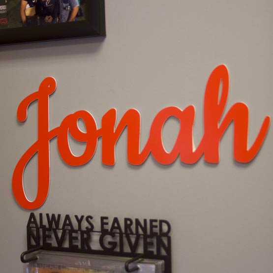 Custom Plastic Sign With Cursive Letters Cutout Of Jonah Name Hanging On Living Room Wall Near Picture Frame And Calendar