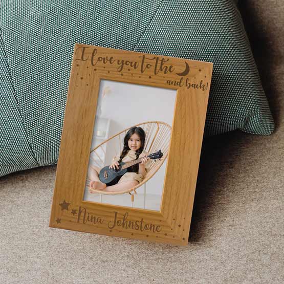 Red Alder Picture Frame With Photo Of Girl Playing Ukulele And Engraved With I Love You To The Moon And Back On Rug By Pillow